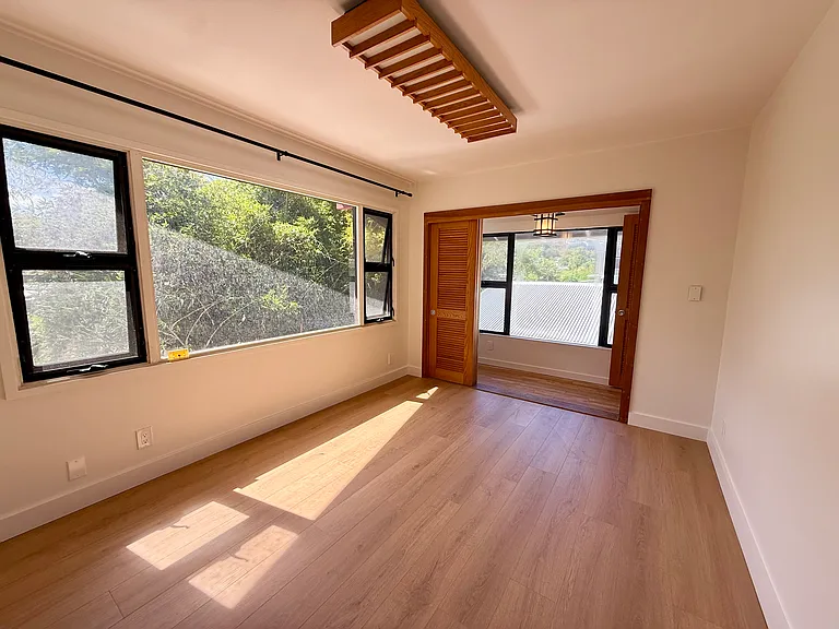 Bright bedroom with large windows overlooking the scenic stream and lush surroundings.