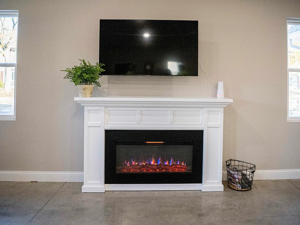 Modern living room with elegant white fireplace and mounted TV, featuring cozy electric flames and fresh greenery.
