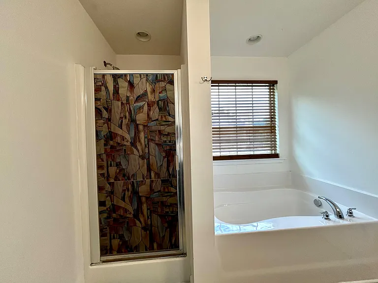 Bathroom with a tub/shower combo, tiled surround, and a window with blinds for ventilation and natural light.