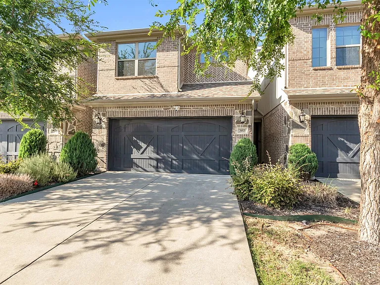 Brick facade townhome featuring an attached garage with a carriage-style door, concrete driveway, and mature landscaping