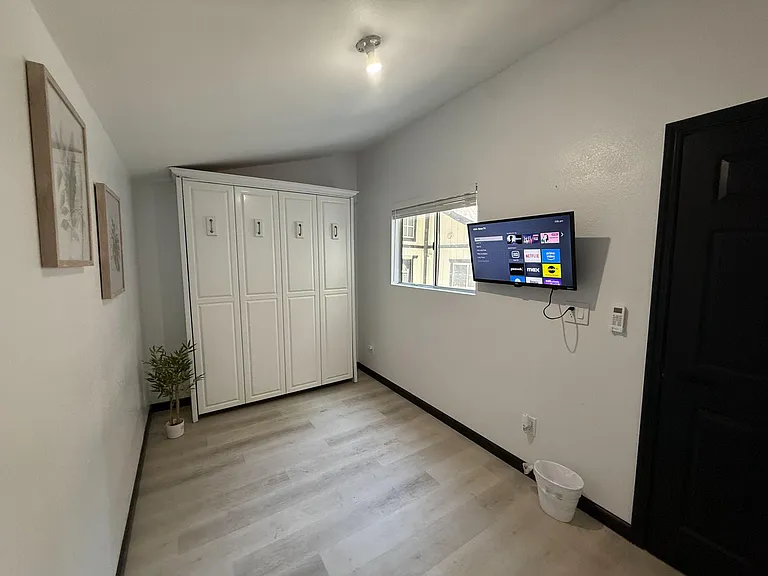 Private bedroom with wide-plank flooring, generous wardrobe storage, and a wall-mounted TV near the window.