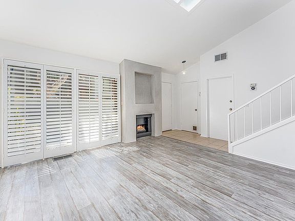 Light, bright, airy living room with skylight, grey driftwood floors, modern gas fireplace and opening through glass sliding door to private patio.