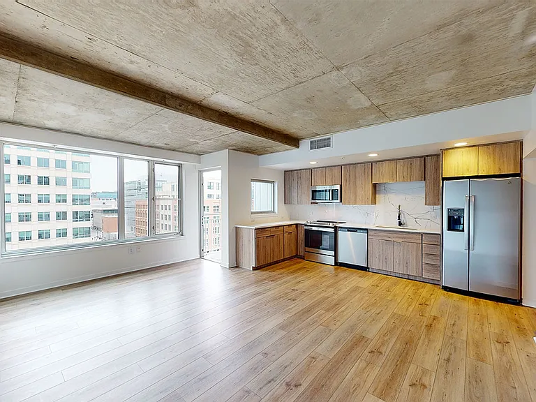 Apartment kitchen with stainless steel appliances, dining and living room with wood-style flooring.