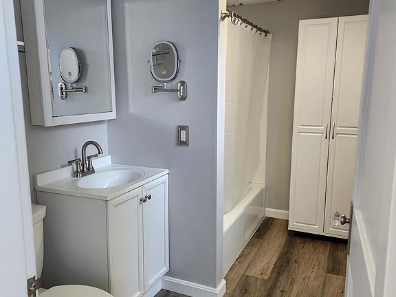 Large full bathroom with wall mounted lit magnifying mirror and storage cabinet