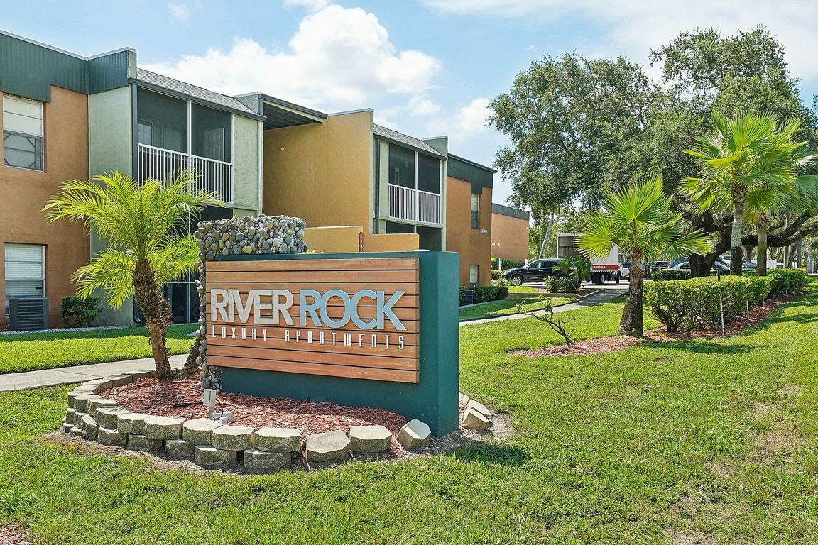 Inviting entrance to River Rock Luxury Apartments with lush greenery and modern signage.