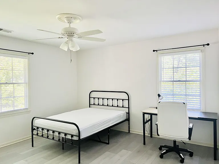 Private bedroom with two large windows, ceiling fan, and space for a bed plus a dedicated desk setup for work or study.