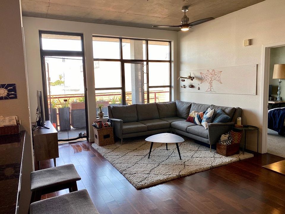 Living room space large enough for sectional sofa. Floor to ceiling windows, ceiling fan, and doorway to private patio.