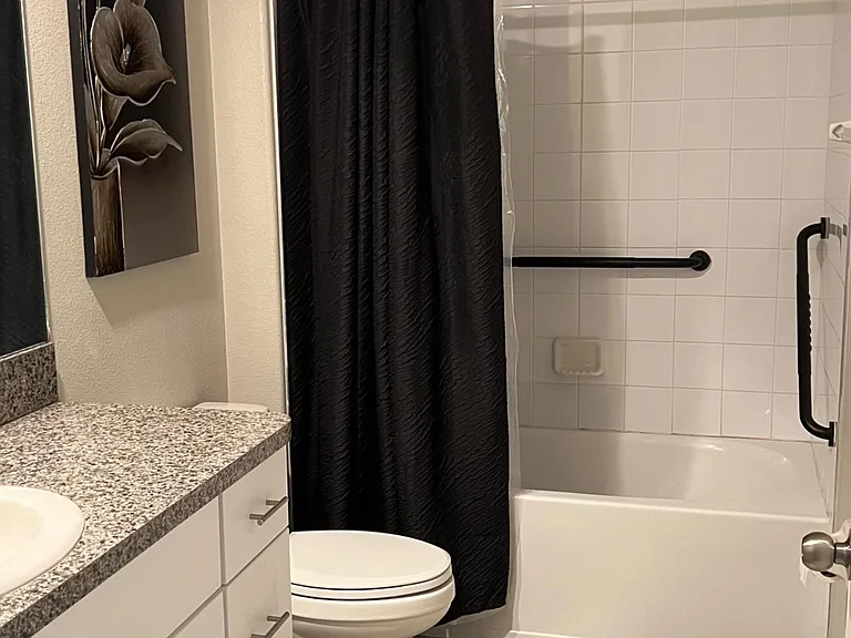 Full bathroom with a tiled tub/shower, spacious vanity with storage, and easy-care tile flooring for daily convenience.