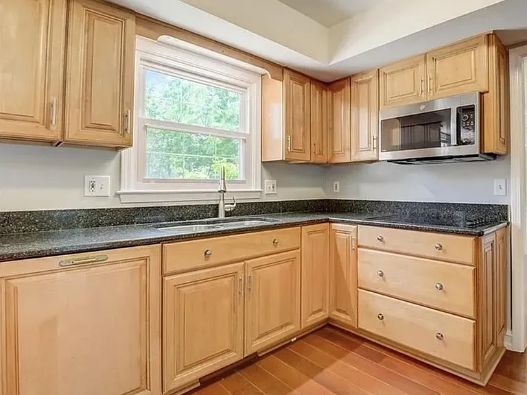Efficient L-shaped kitchen with ample wood cabinetry, granite-look counters, and a window over the sink plus built-in microwa
