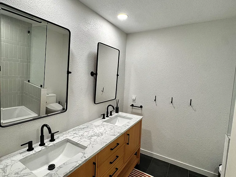 Beautifully remodeled hallway bathroom featuring a custom dual-sink vanity, quartz countertops, designer tile surround, modern fixtures
