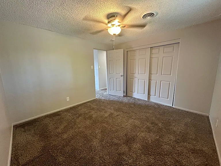 Inviting bedroom with plush carpet, ceiling fan, and ample closet space in modern apartment. Inviting bedroom with plush carpet, ceiling fan, and ample closet space in modern apartment.