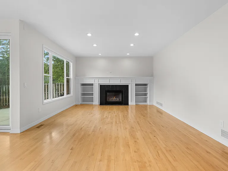 The spacious living room features a cozy gas fireplace with built-in shelving, expansive windows overlooking the backyard, and plenty of wall space for a large TV or additional seating arrangements.