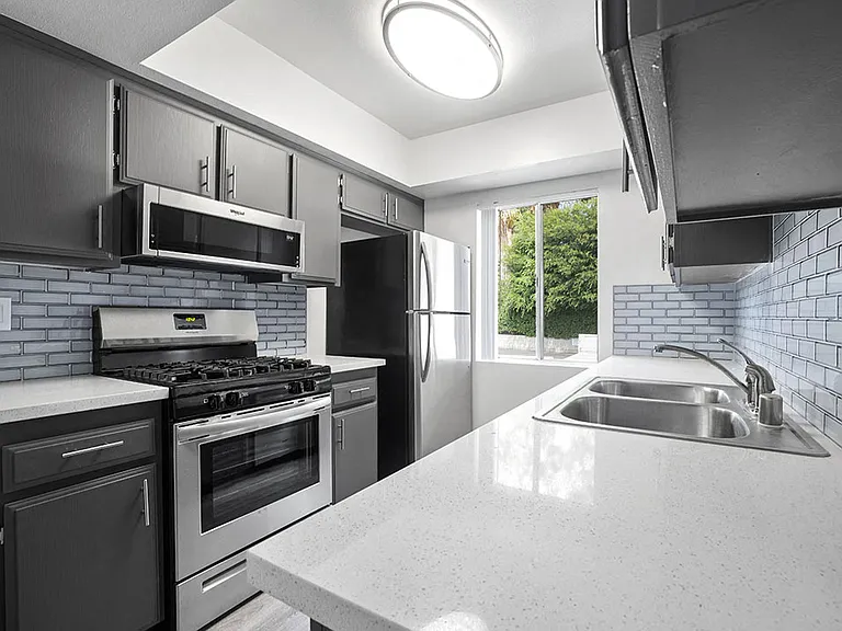 Tiled kitchen with stainless steel oven, microwave, and fridge.