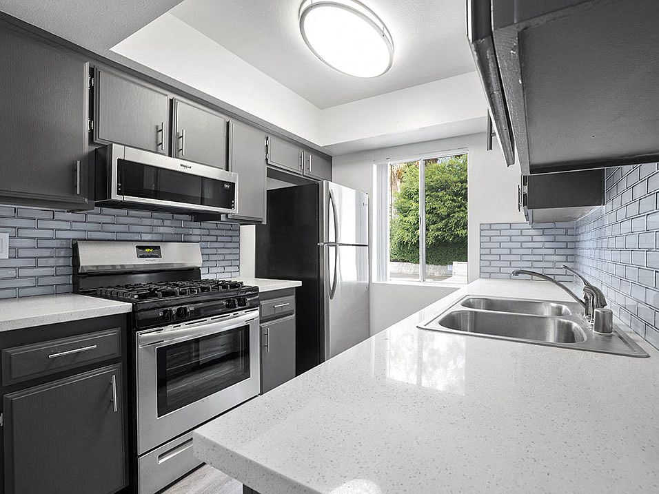 Tiled kitchen with stainless steel oven, microwave, and fridge.