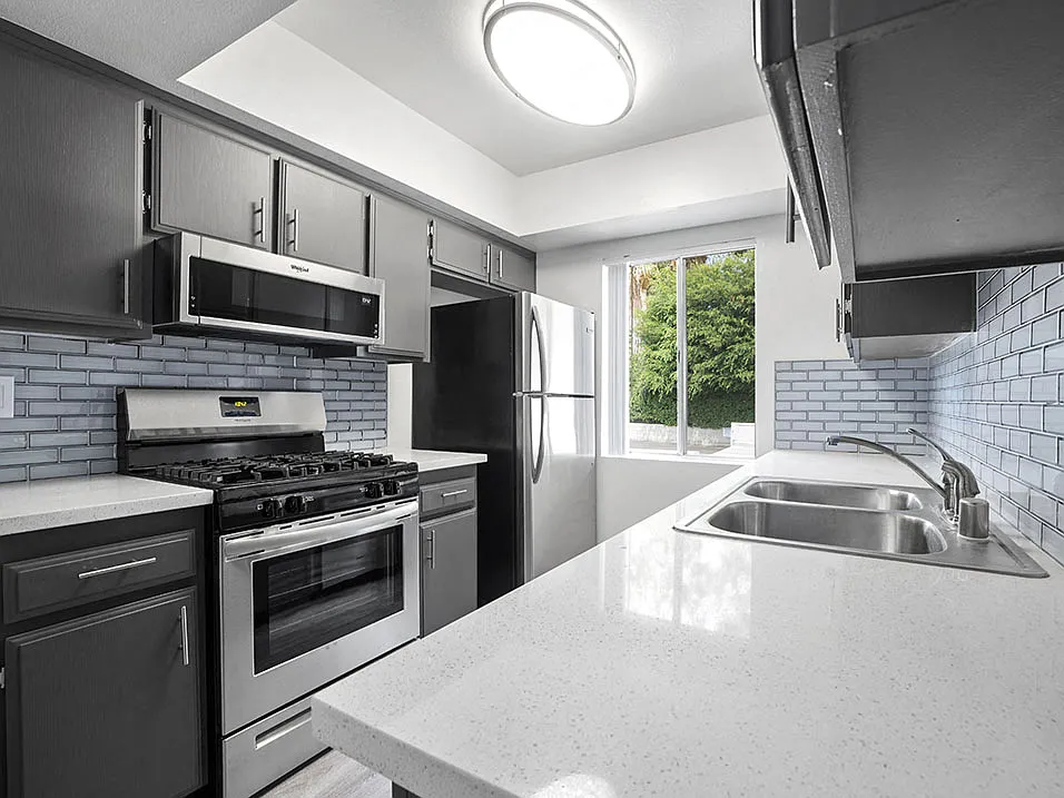 Tiled kitchen with stainless steel oven, microwave, and fridge.