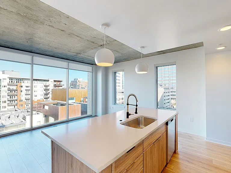 Apartment kitchen with stainless steel appliances, dining and living room with wood-style flooring.