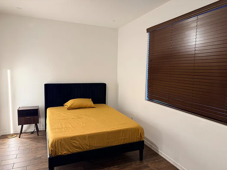 Private bedroom with a Queen bed, nightstand, and wood-style flooring, plus a large window with blinds for light control.