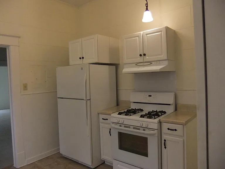 Kitchen with gas oven and stove and hood, cabinets and refrigerator.