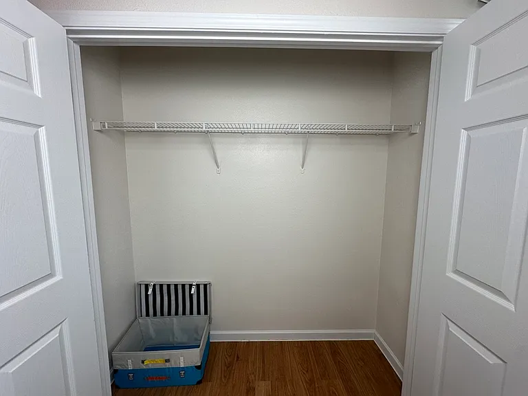 Spacious closet with wooden flooring and a built-in wire shelf, offering ample storage space. Spacious closet with wooden flooring and a built-in wire shelf, offering ample storage space.