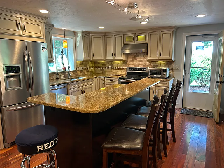 Large Chefs Kitchen with center island and stainless-steel appliances, granite counters and hardwood flooring throughout.