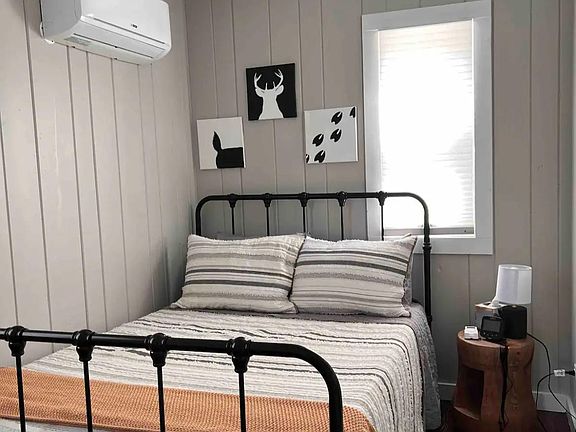 Primary bedroom with full sized bed with ceiling fan and wall AC unit.