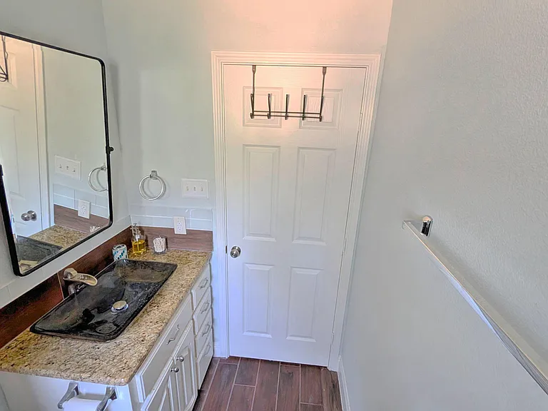 Half bath with granite-top vanity, vessel sink, framed mirror, and wall hooks for daily convenience.