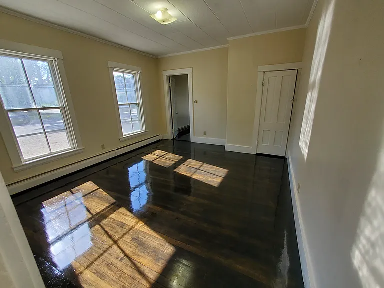 Living room has mini blinds on the windows and a hardwood refinished floor