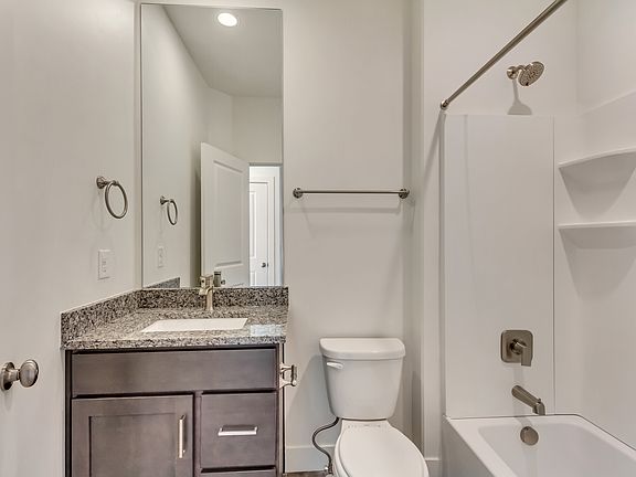 Modern bathroom with a granite countertop, dark wood vanity, large mirror, and shower-tub combo with