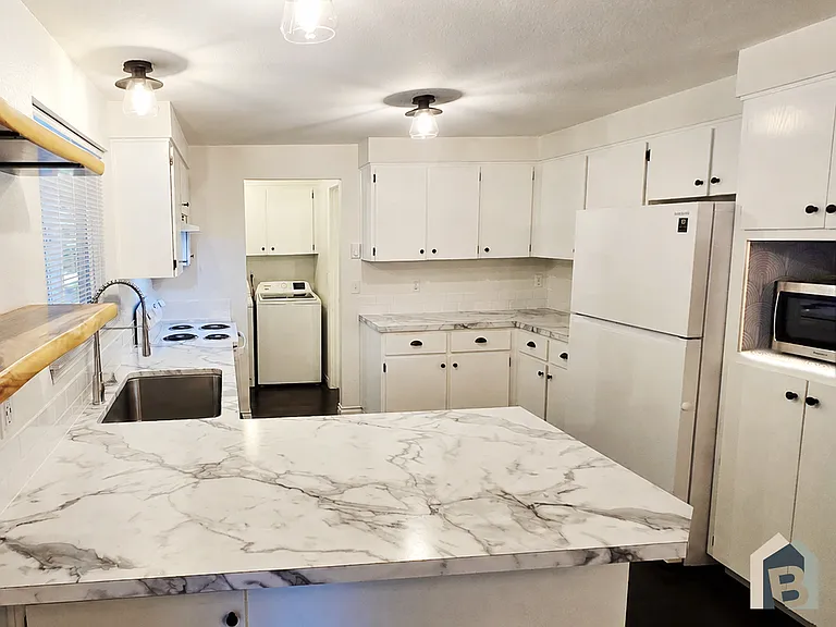 Kitchen with brand new countertops, stove, sink, faucet, microwave, & backsplash.