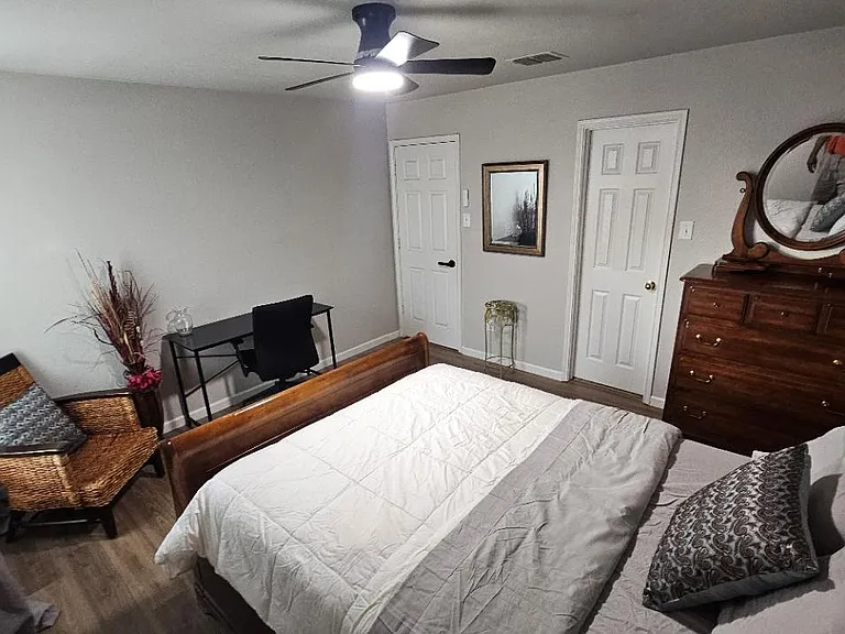 Furnished bedroom featuring a bed, dresser with mirror, desk workspace, and ceiling fan, plus convenient closet access.