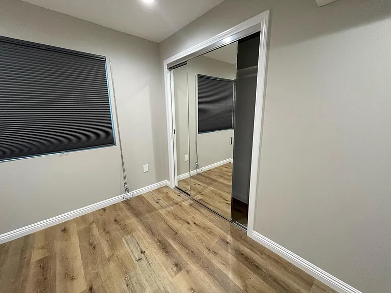 Mirrored closet sliding door in bedroom. and window with shade.
