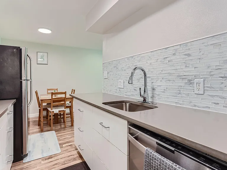 Updated galley kitchen with stainless appliances, tile backsplash, ample cabinetry, and a nearby dining nook.