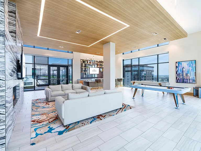 Resident lounge with open seating, a game table, and floor-to-ceiling windows, balancing social energy with room to unwind.