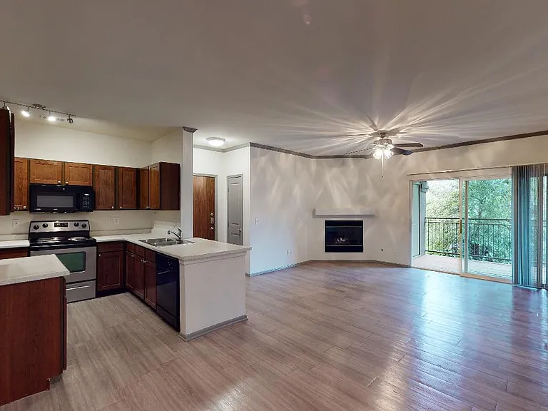 Apartment kitchen with stainless steel appliances, dining and living room with wood-style flooring, fireplace, and balcony in select homes.