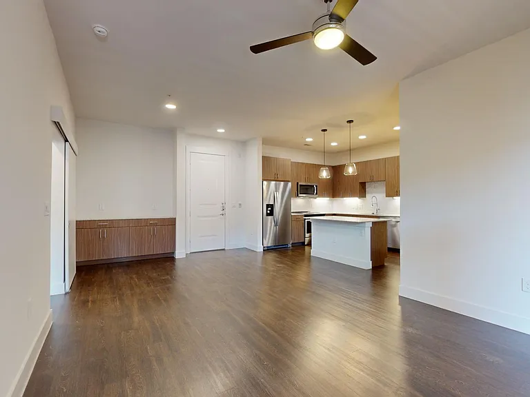 Apartment kitchen with stainless steel appliances, dining and living room with wood-style flooring.