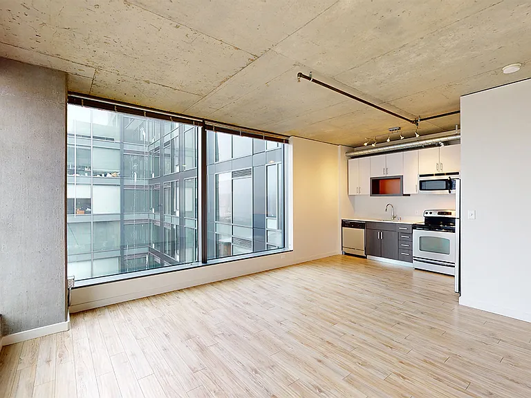 Apartment kitchen with stainless steel appliances, dining and living room with wood-style flooring.