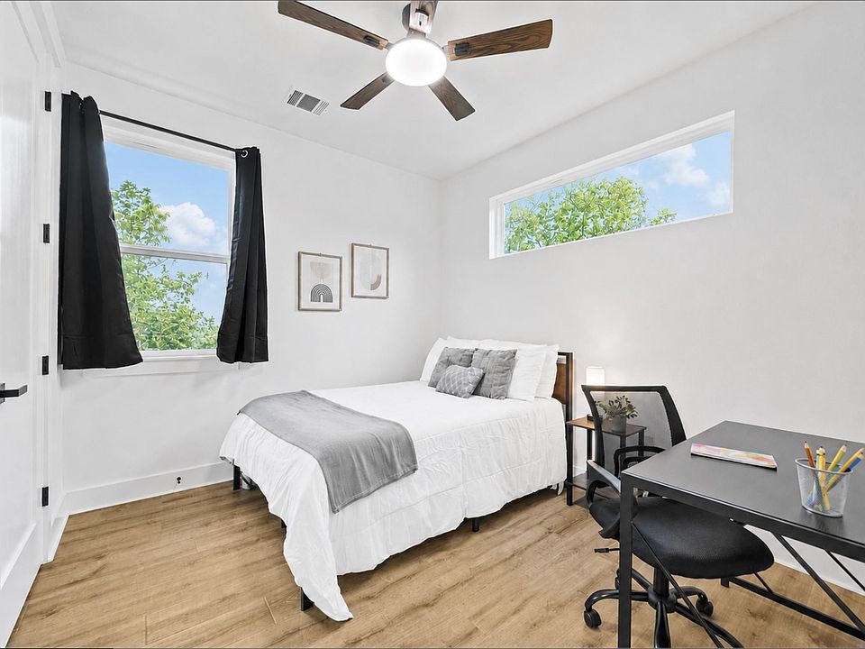 Bedroom with wood-look flooring, ceiling fan, two windows, and space for a bed plus a dedicated desk area.