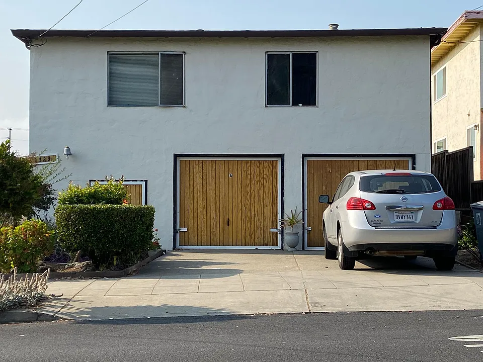 Exterior photo showing off-street parking. The apartment sits behind the garage on the first floor.