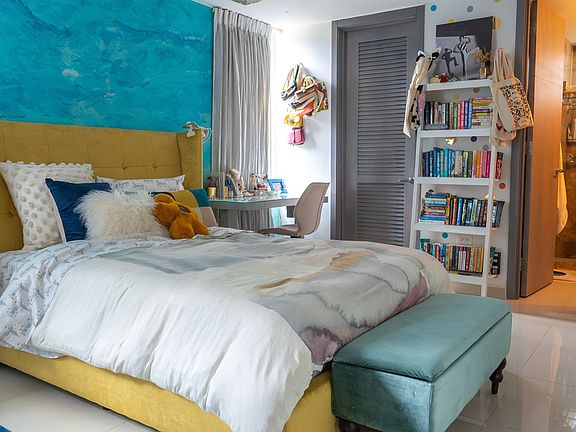 Vibrant bedroom with artistic flair, featuring a bold accent wall, cozy upholstered bed, and custom shelving. A colorful and inspiring space perfect for rest and creativity.