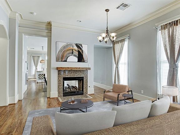Living room has gleaming hardwood floors, decorative crown moulding, and a unique two-sided fireplace. Closet and half bathroom are through the arch to the left. This picture has been virtually staged.