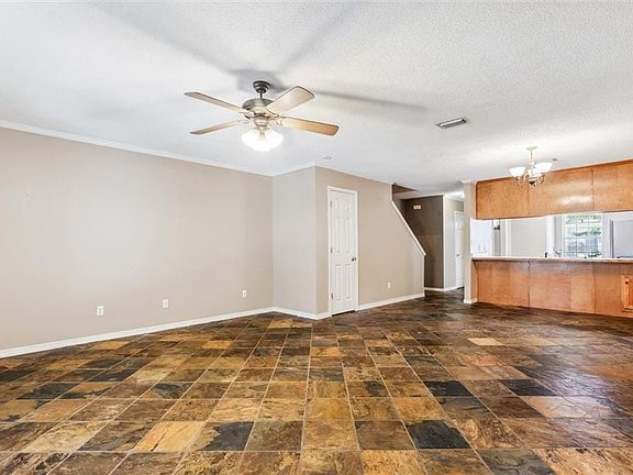 Unfurnished living room with a textured ceiling, dark tile patterned floors, ceiling fan with notable chandelier, and ornamental molding