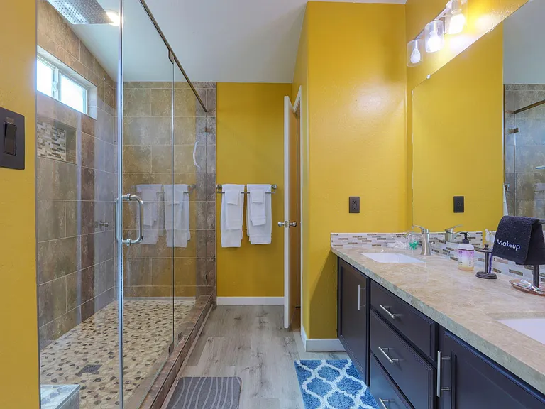 Spacious bath with a glass-enclosed walk-in shower, long vanity with ample storage, and bright wall mirror lighting.