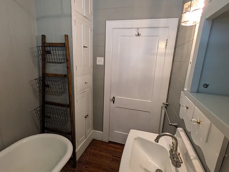 Bathroom has full height storage cabinet and storage rack at end of tub for easy access to shower supplies.