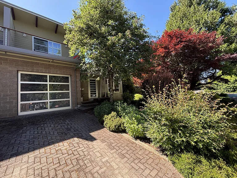 Front of the house including paver driveway, garage door, upstairs balcony, front yard landscaping with privacy and shade.