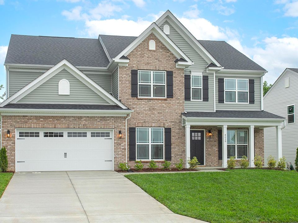 Two-story suburban house with gray siding, brick accents, black shutters, a two-car garage, and a ma