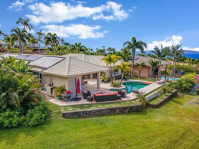 View of home from rear open landscape area with view of pool, BBQ, umbrella and seating.