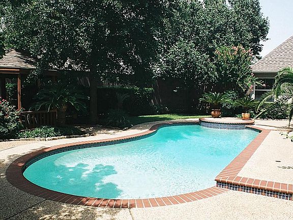 Freeform kidney-shaped pool with tile coping and exposed-gravel walkways surrounded by luscious tropical greenery.