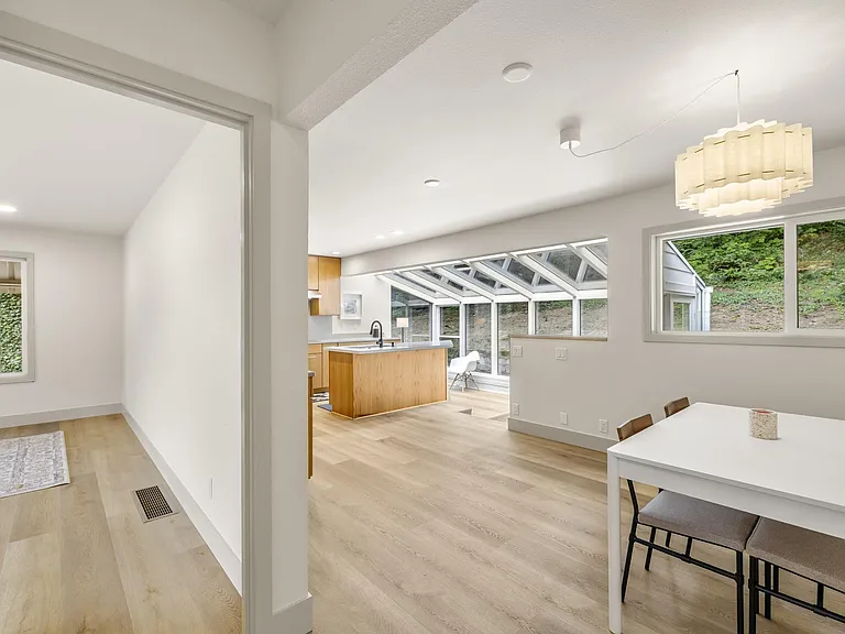 Open dining area flows into the kitchen and sunroom, featuring large windows, wood floors, and space for a full table.