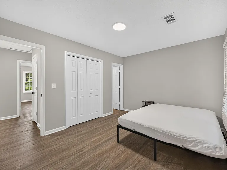 Spacious bedroom with wood-style flooring, a large double-door closet, and a window with blinds for easy light control.