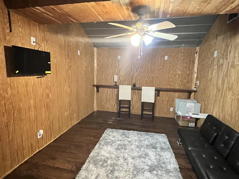 Flexible common room with mounted TV, ceiling fan, and open floor space for lounge seating or a small work area.
